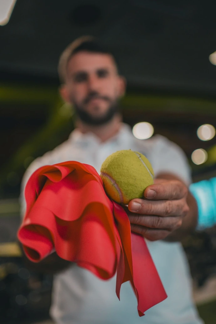 A man holding a tennis ball and a red ribbon